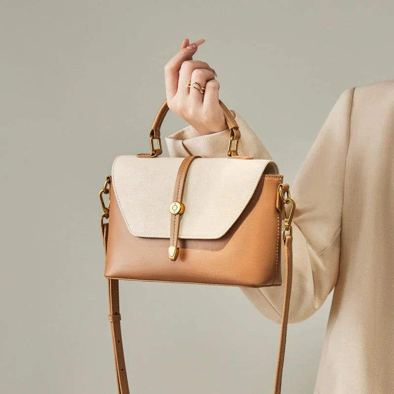 Woman holding a beige and tan leather crossbody handbag with gold hardware