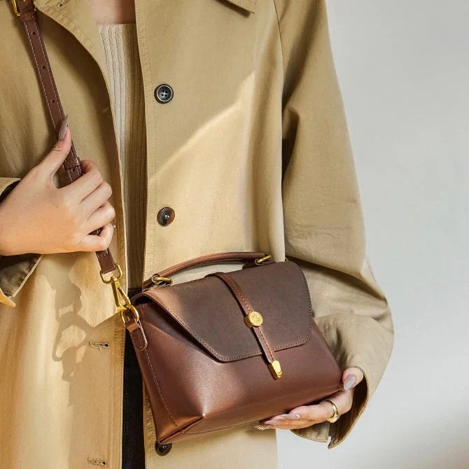 Woman in beige coat holding elegant brown leather handbag with gold hardware