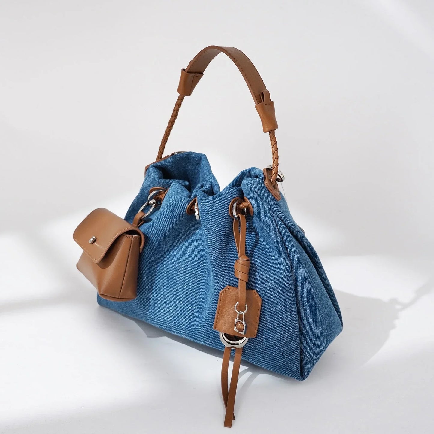 Blue denim handbag with brown leather handle and pocket, stylish purse on white background