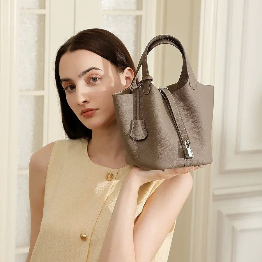 Woman in beige dress holding taupe leather bucket handbag indoors