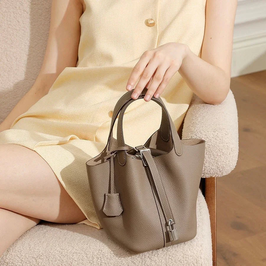 Taupe leather handbag on woman's lap in beige dress, sitting on cream chair indoors