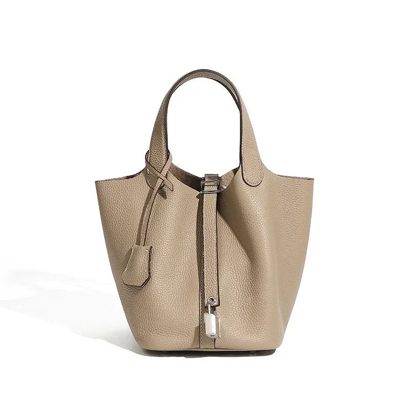 Taupe leather tote bag with pebbled texture and silver lock accent on white background