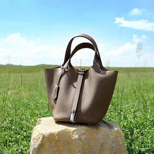Taupe leather handbag on a stone with green grass field and blue sky background