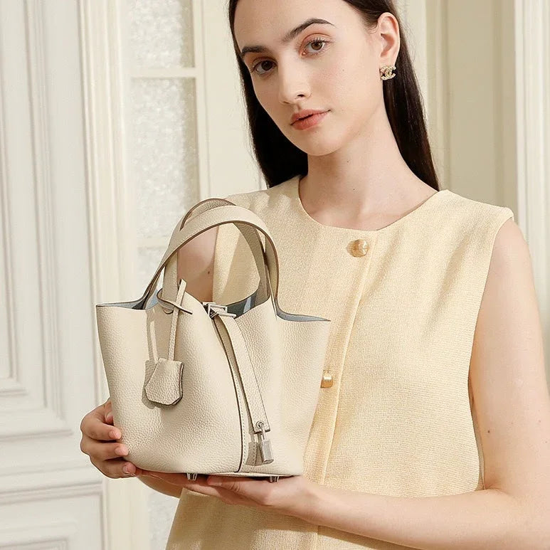 Woman holding a cream leather bucket bag in a light-colored room, minimalist fashion style
