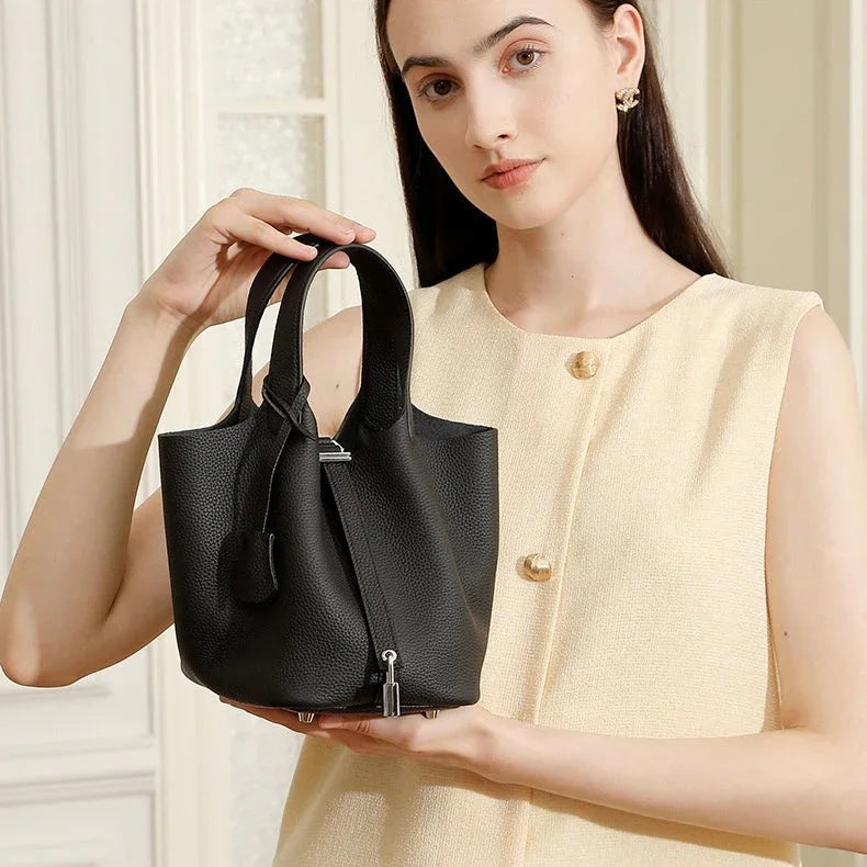 Woman in cream sleeveless top holding black leather bucket bag in bright indoor setting