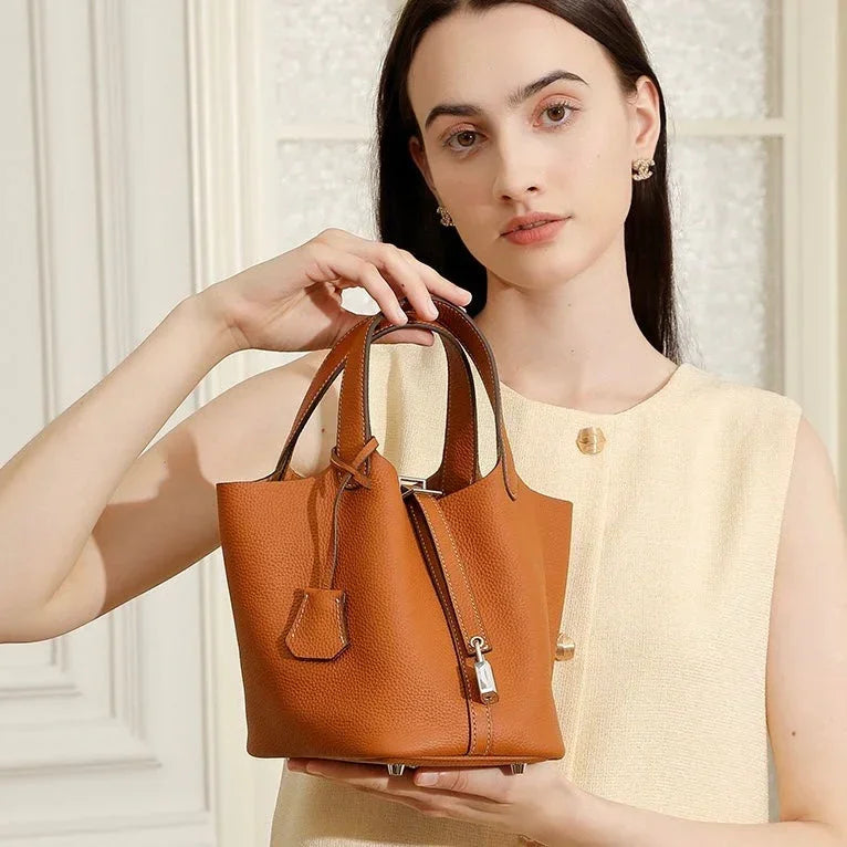 Woman in beige dress holding brown leather bucket handbag with top handles indoors