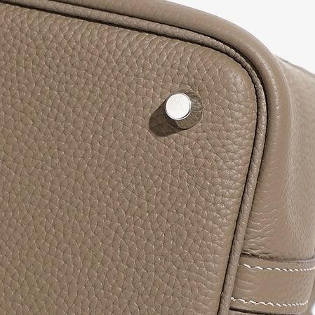 Textured taupe leather bag corner with metal stud and white stitching detail