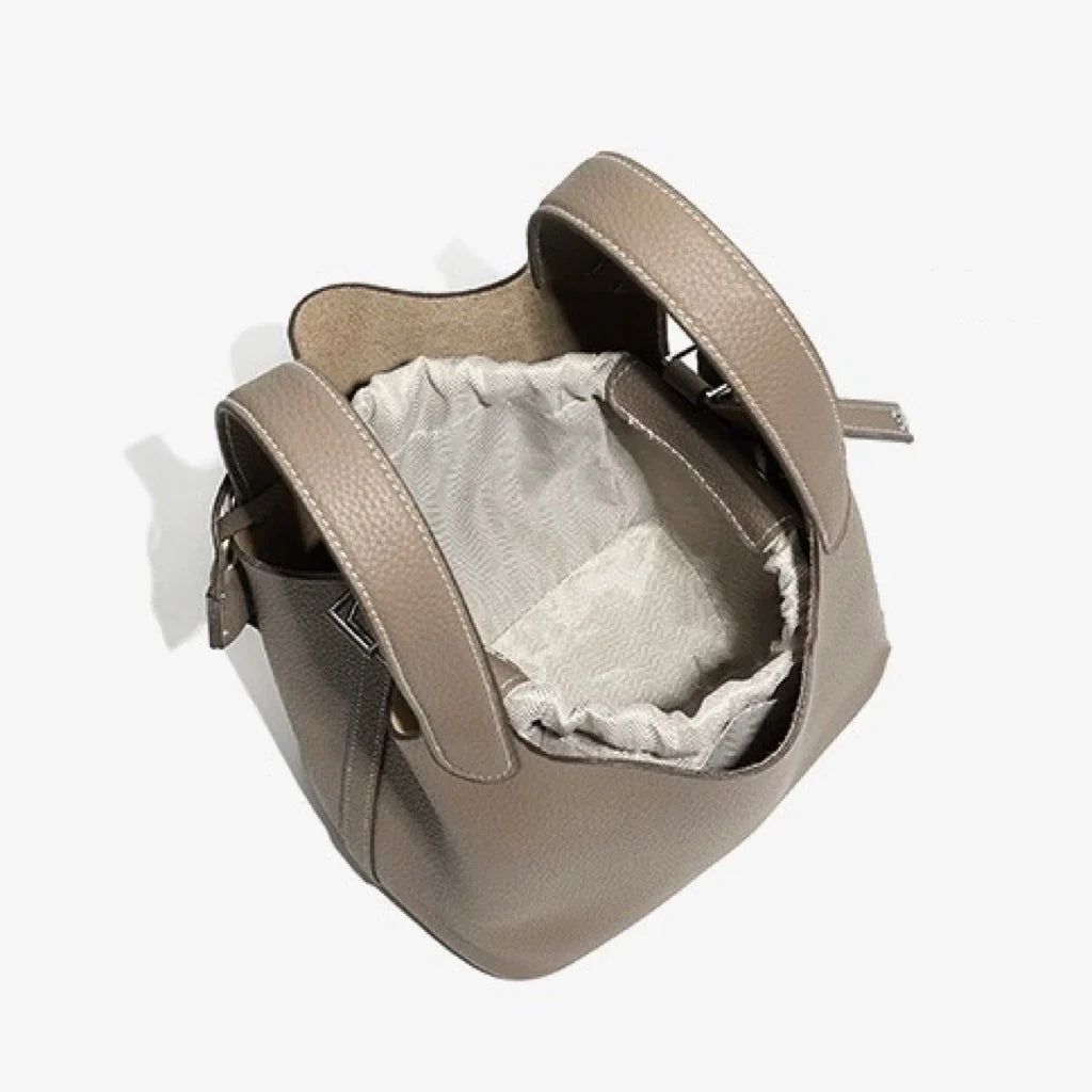 Taupe leather bucket bag with drawstring closure and textured handles on white background