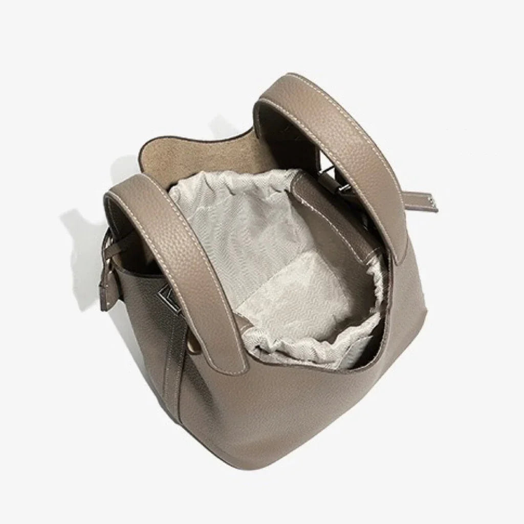 Taupe leather bucket bag with drawstring closure and textured handles on white background