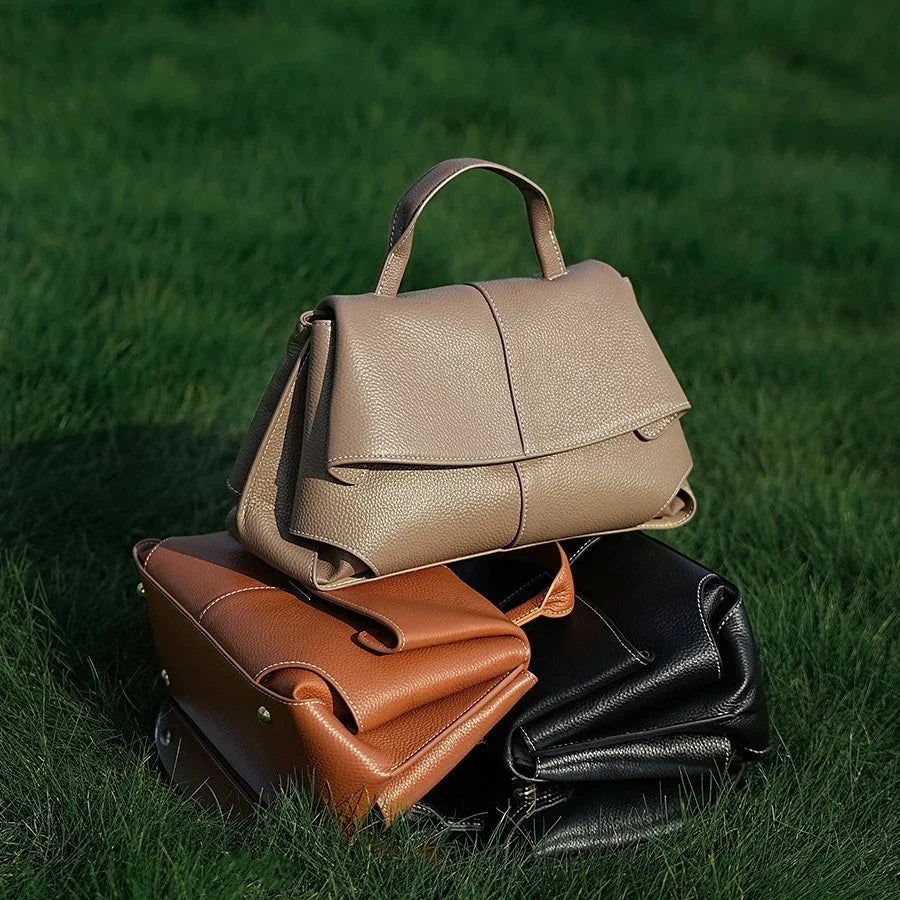 Three leather handbags in beige, brown, and black on green grass outdoors