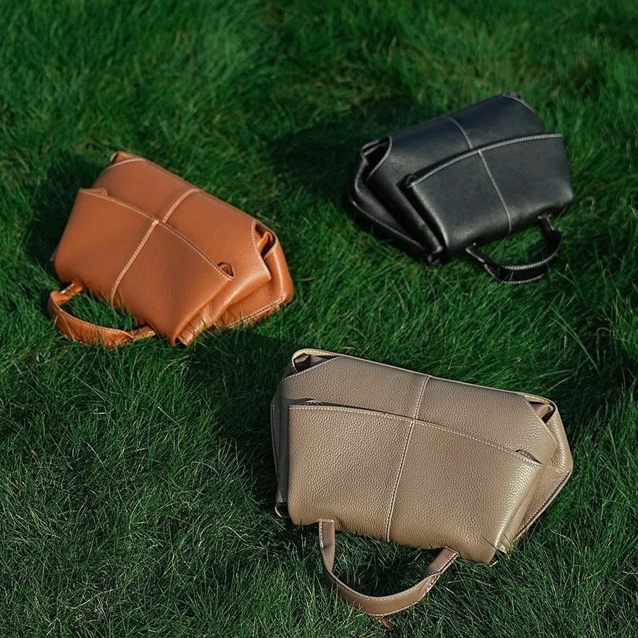 Three leather handbags in tan, black, and beige on green grass outdoor setting