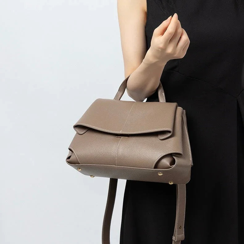 Woman in black dress holding taupe leather handbag with top handle and shoulder strap