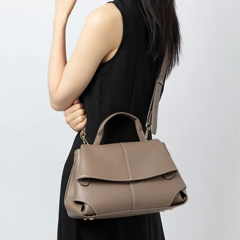 Taupe leather handbag with top handle and shoulder strap on woman in black dress