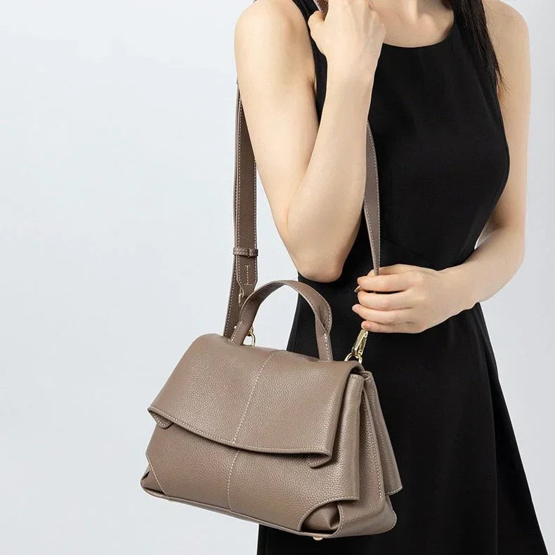 Woman in black dress holding taupe leather handbag with top handle and shoulder strap
