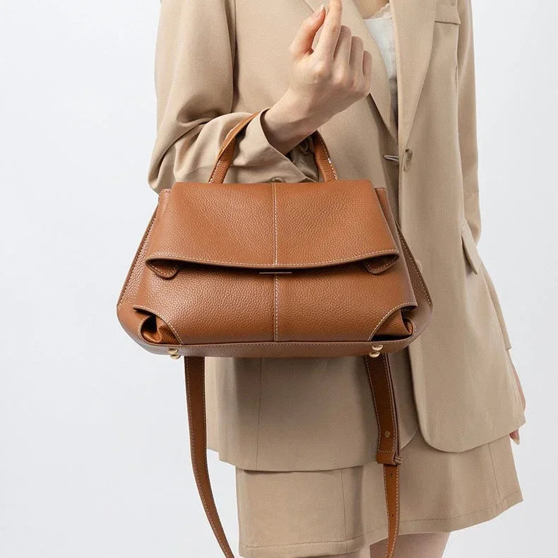Woman in beige suit holding a stylish brown leather handbag with top handles