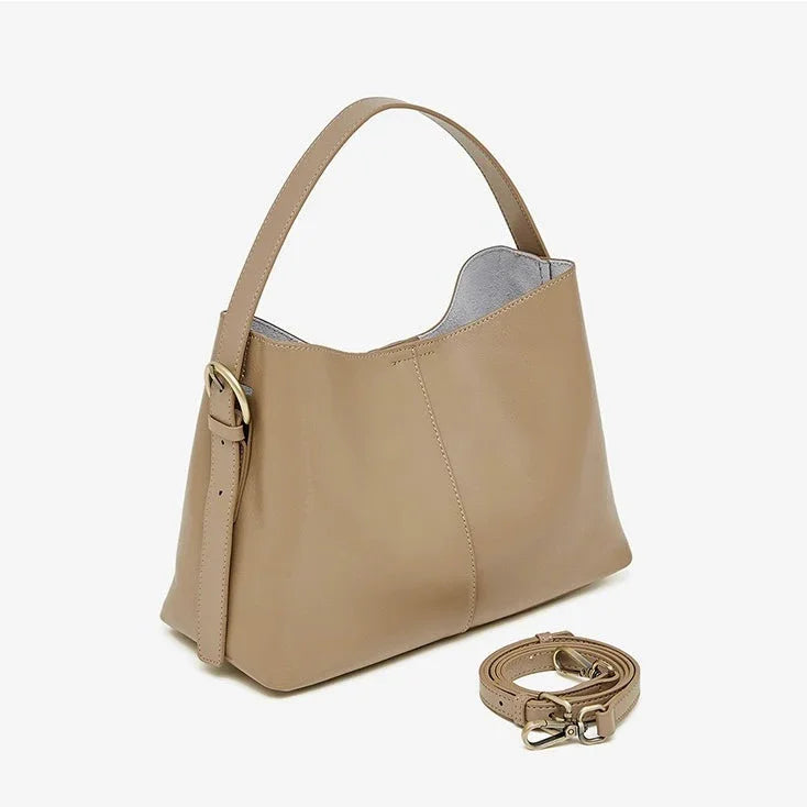 Beige leather shoulder bag with gold buckle and detachable strap on white background