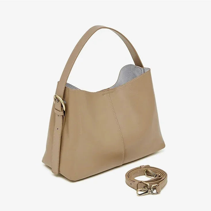 Beige leather shoulder bag with gold buckle and detachable strap on white background