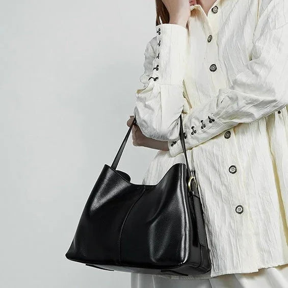 Woman in textured white blouse holding black leather tote bag on shoulder