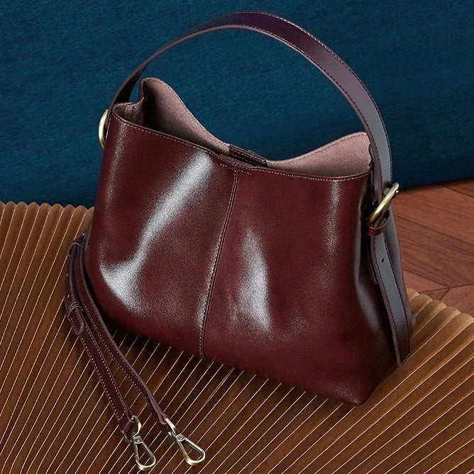 Burgundy leather shoulder bag with gold hardware and detachable strap on a brown surface