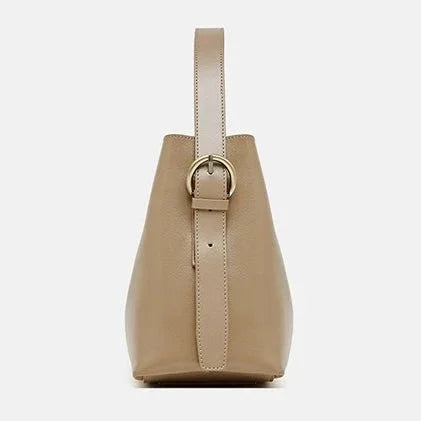 Side view of beige leather handbag with strap and gold buckle on white background