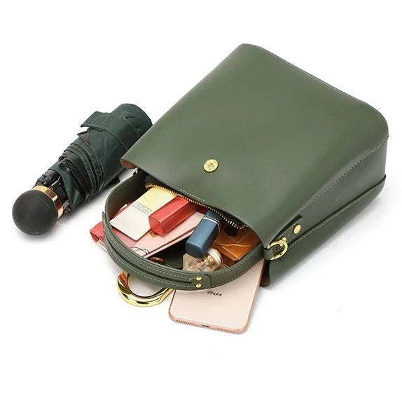 Green leather handbag with gold accents, open to show contents and a closed umbrella beside it