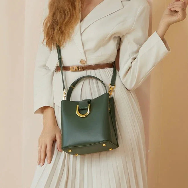 Woman in cream dress with brown belt holding green leather handbag with gold hardware
