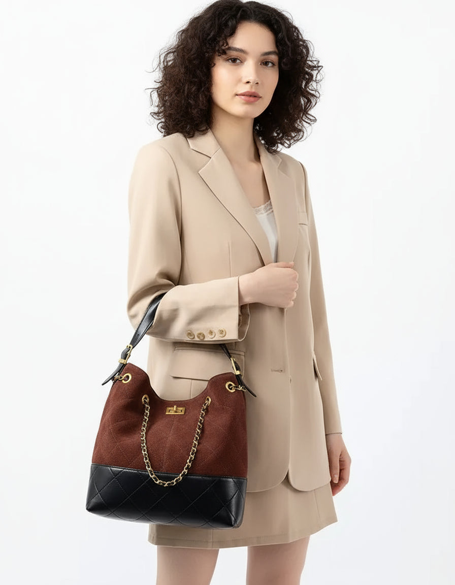 Woman in beige blazer holding a brown and black quilted leather shoulder bag with chain strap
