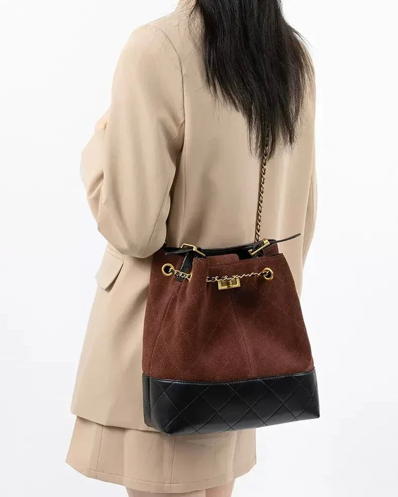 Woman in beige blazer carrying brown suede and black leather bucket bag with gold chain strap