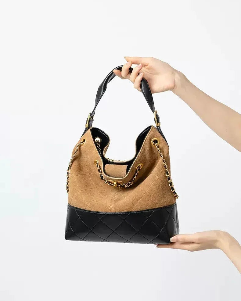 Brown and black leather shoulder bag with chain strap held by hands on white background.