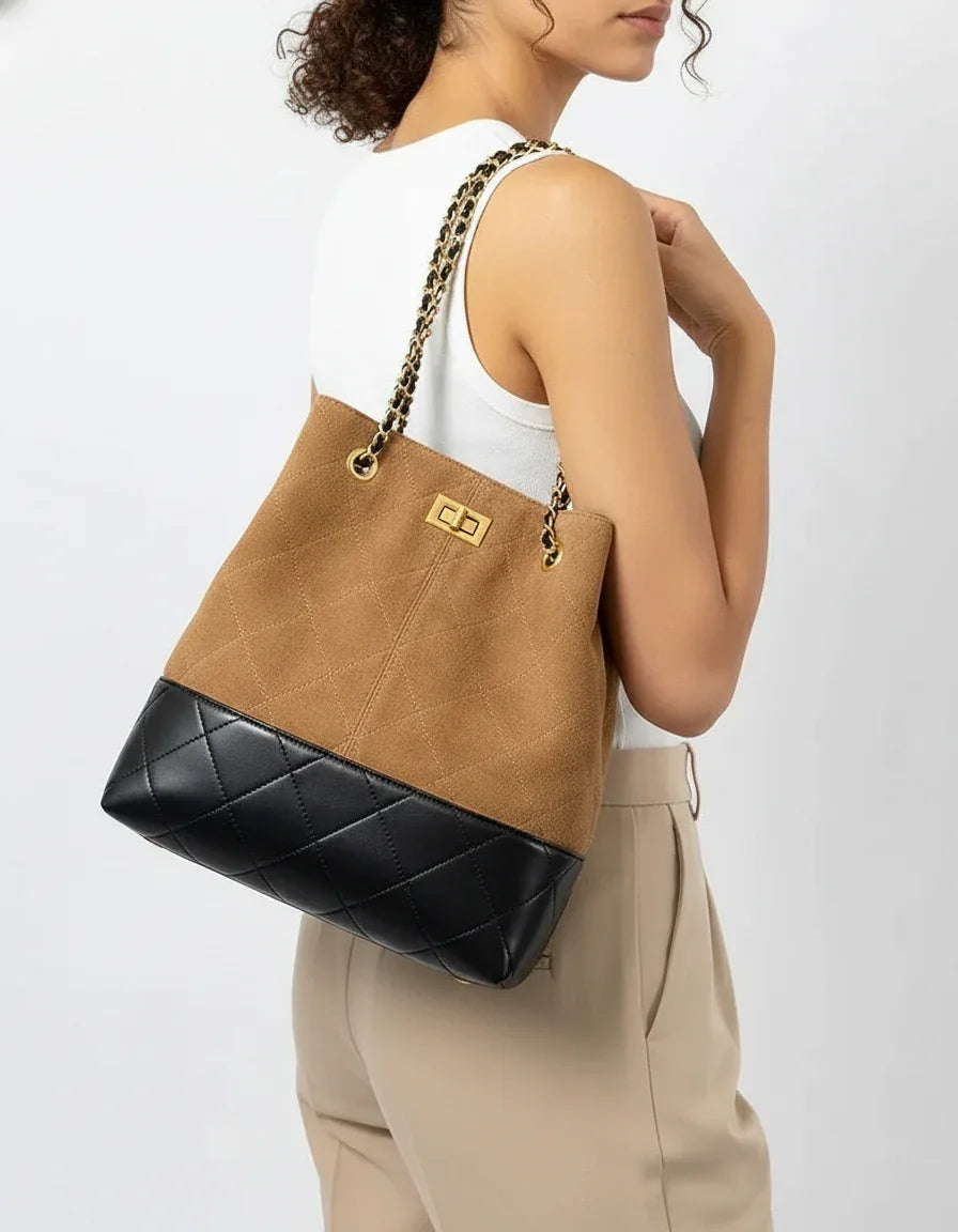 Woman wearing a tan and black quilted bucket bag with gold chain strap