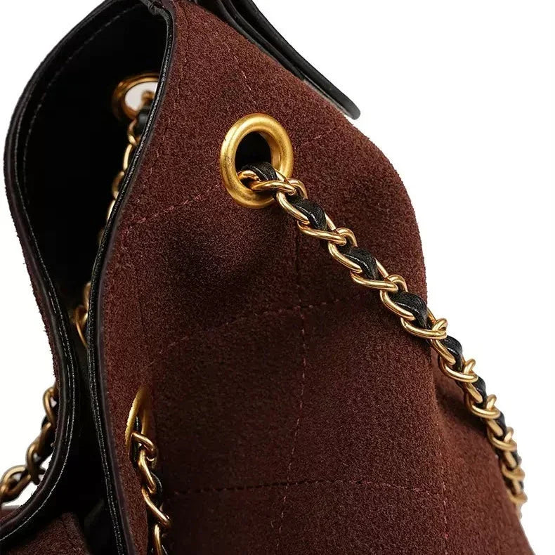Brown suede handbag with gold chain strap and grommet detail, close-up view