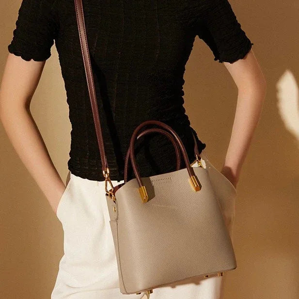 Woman wearing black top and white pants with beige leather handbag and brown strap