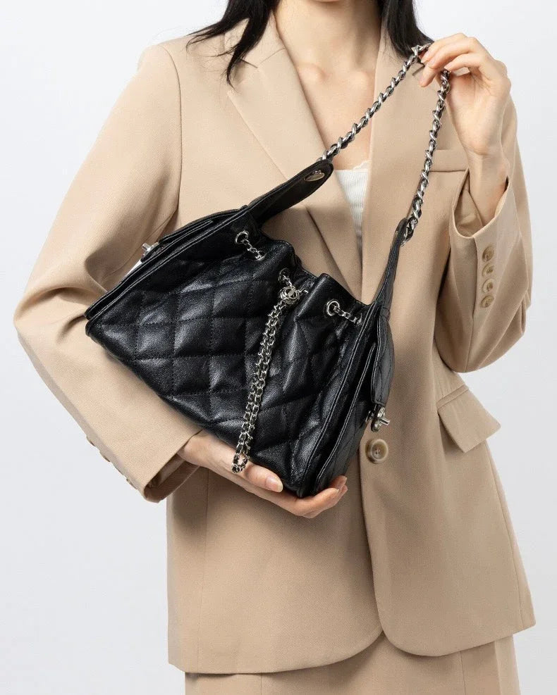 Woman in beige blazer holding black quilted leather handbag with chain strap