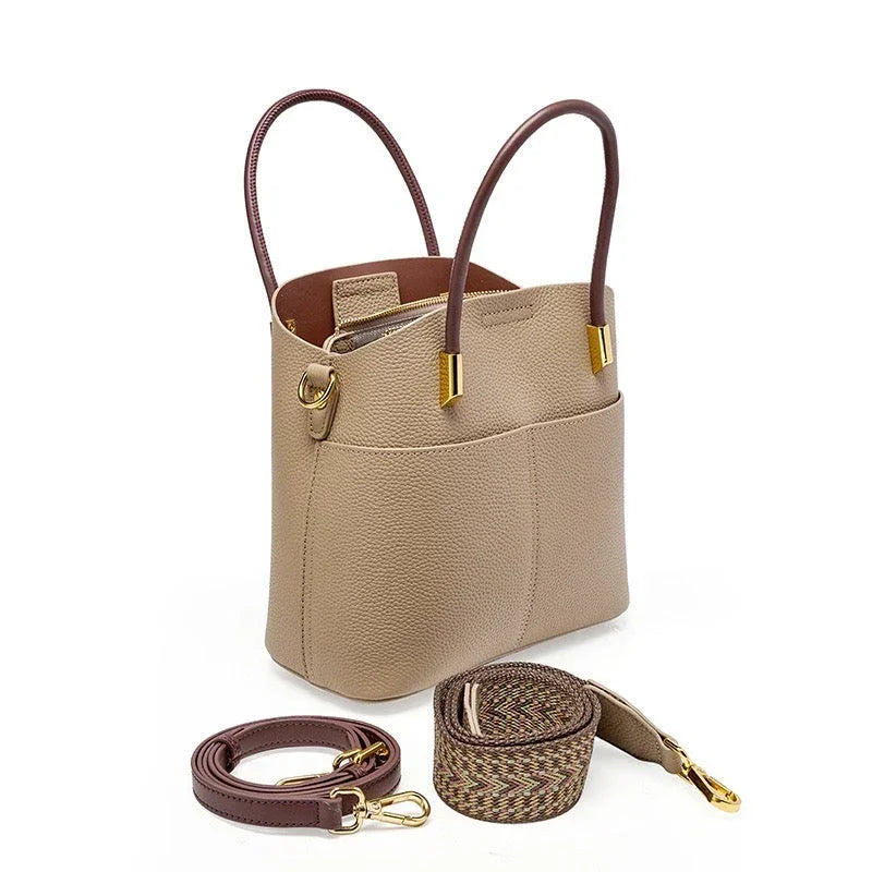 Beige leather tote bag with gold accents, brown handles, and detachable straps on white background