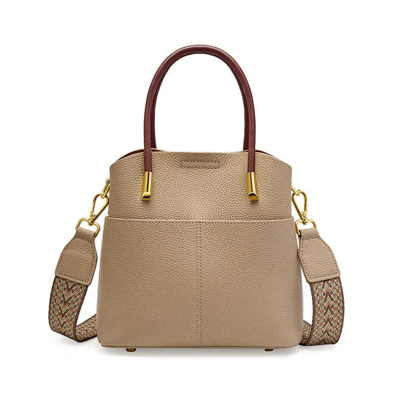 Taupe leather handbag with brown handles, gold hardware, and woven shoulder strap