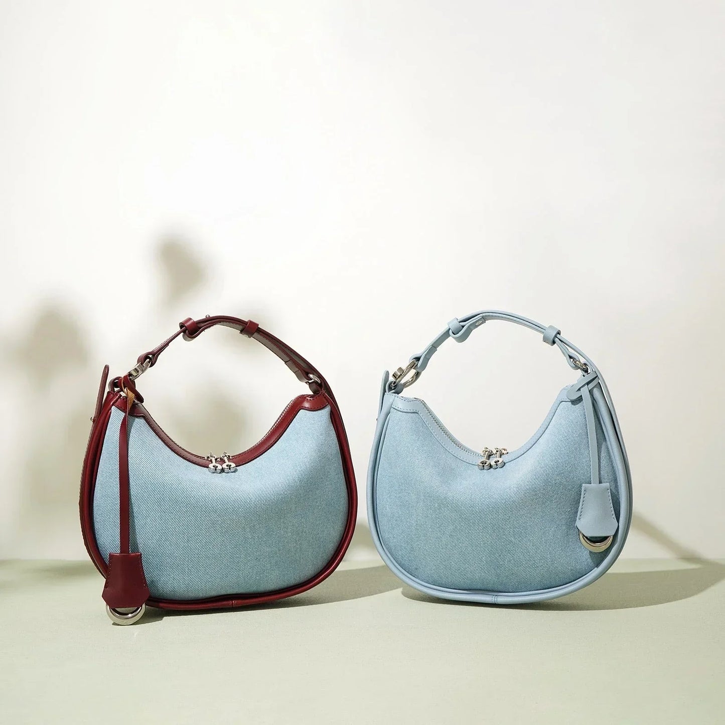 Two crescent-shaped handbags, one with blue and red leather, one all light blue, on neutral background