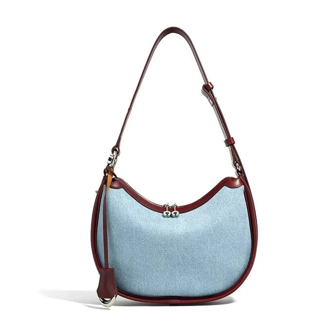 Light blue denim shoulder bag with brown leather trim and adjustable strap on white background