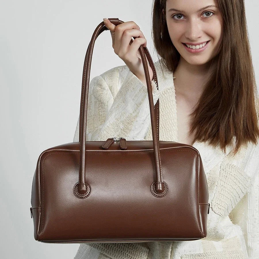 Woman holding a brown leather handbag with double handles, neutral background
