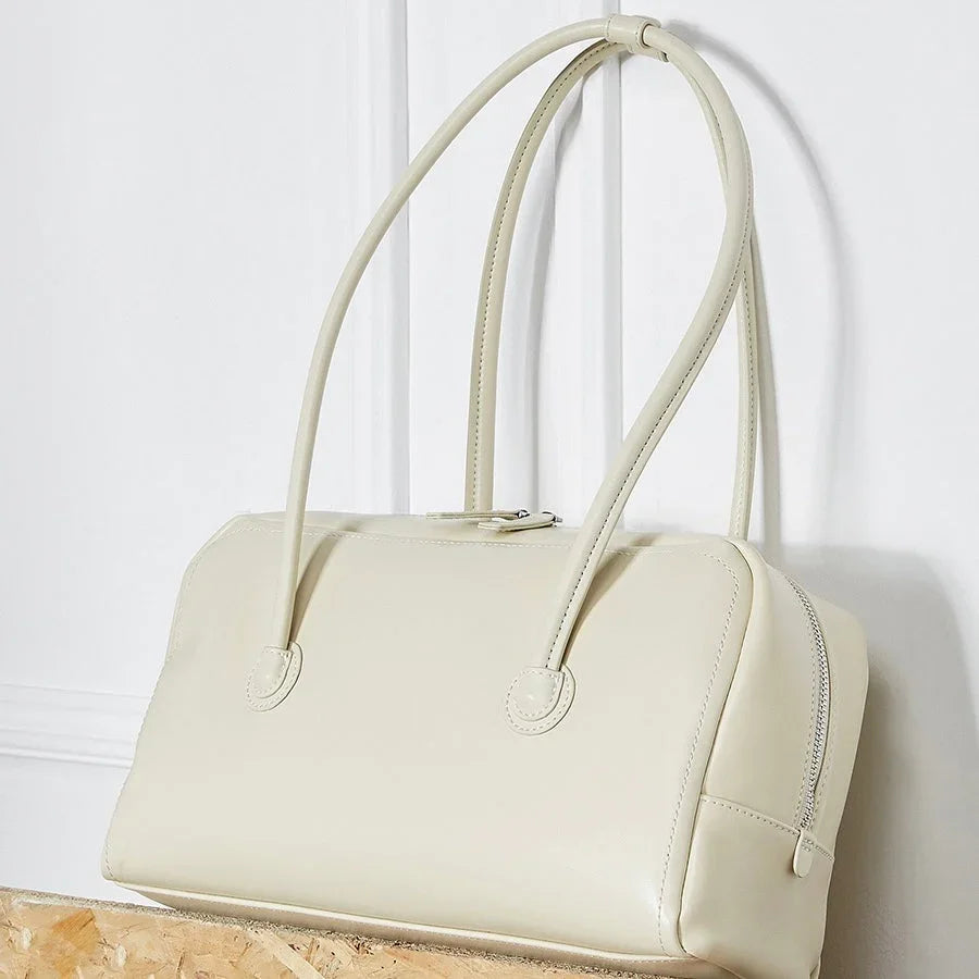 Cream leather handbag with double handles on a light background
