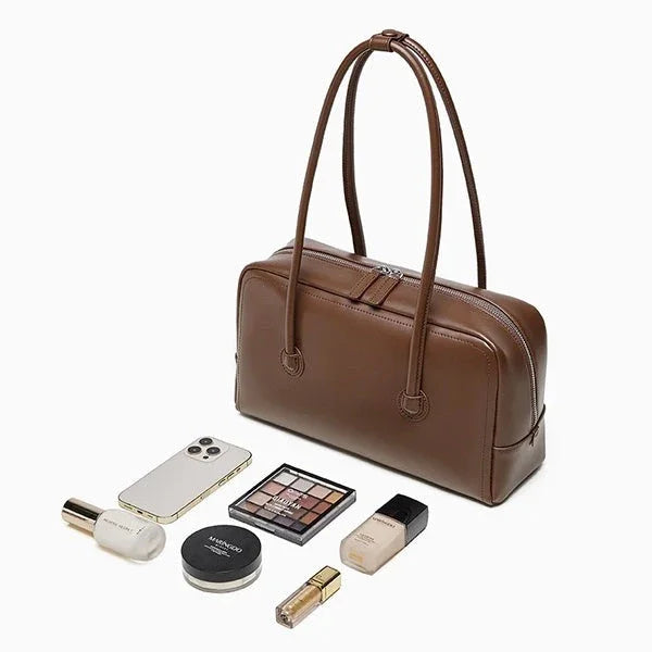 Brown leather handbag with makeup, phone, and beauty essentials on white background