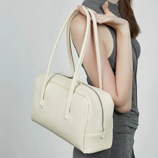 Woman in grey dress holding a cream leather handbag with double shoulder straps