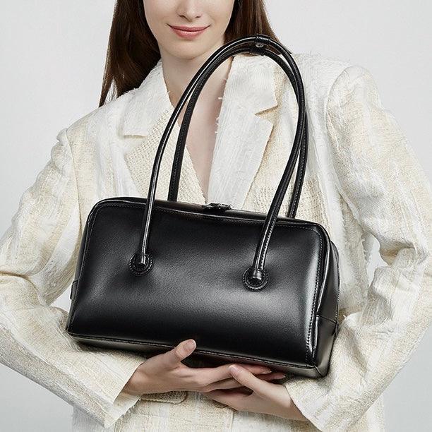 Woman in white blazer holding black leather handbag with double handles
