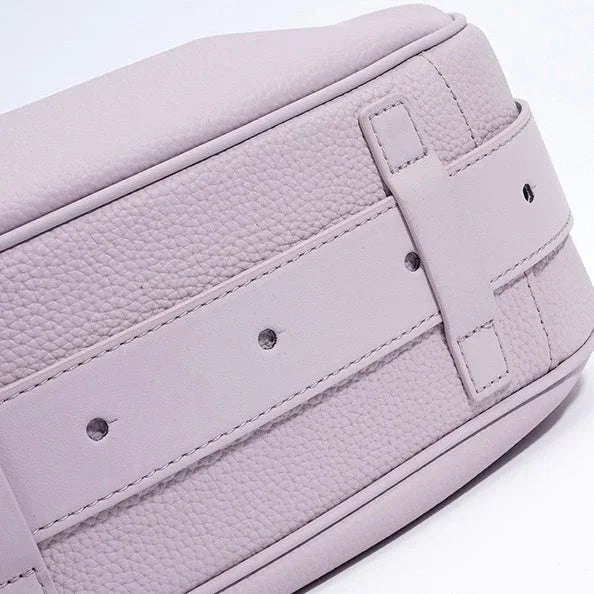 Closeup of a light purple leather bag with textured surface and belt strap detail