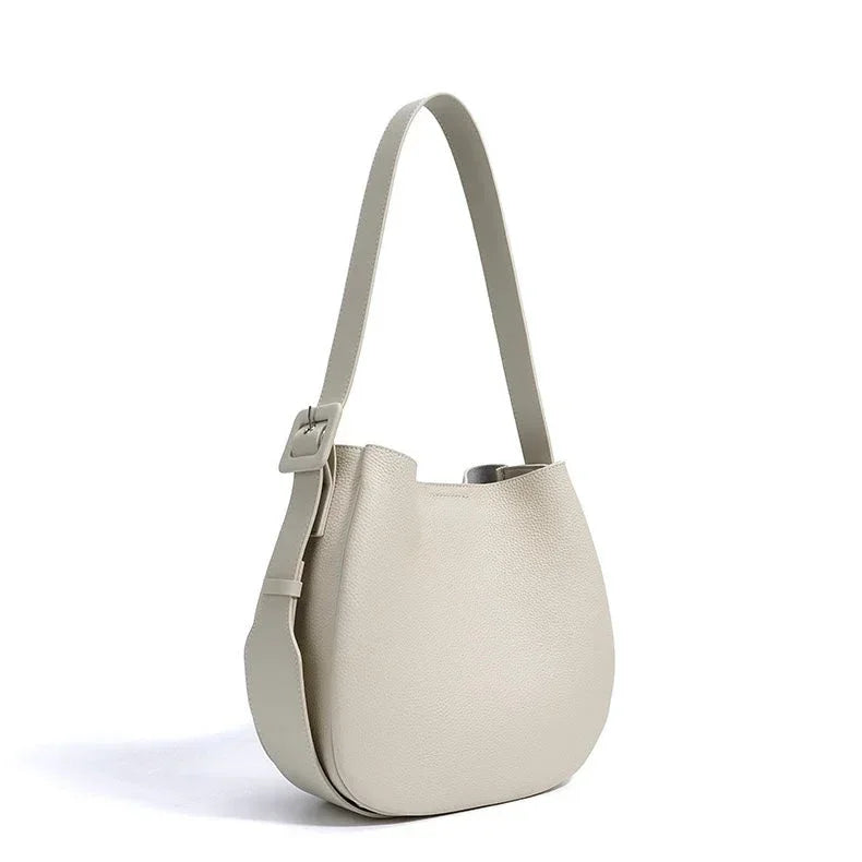 Beige leather bucket bag with wide adjustable shoulder strap on white background