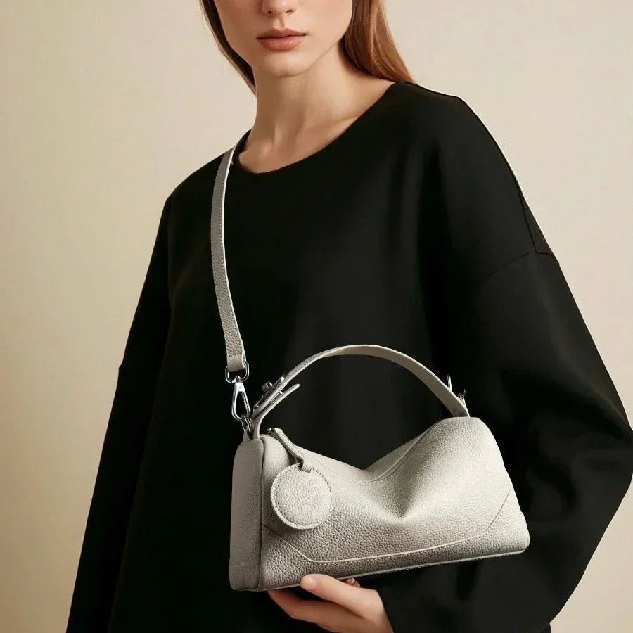 Woman in black top holding a minimalist light gray leather handbag with handle and strap