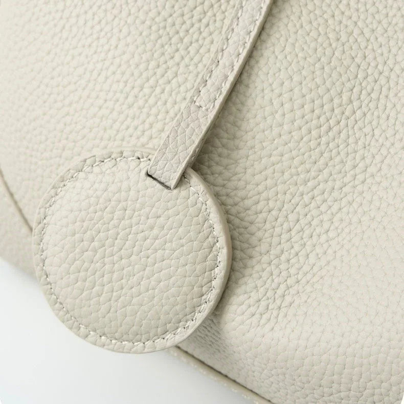 Close-up of textured beige leather handbag with round accent and visible stitching