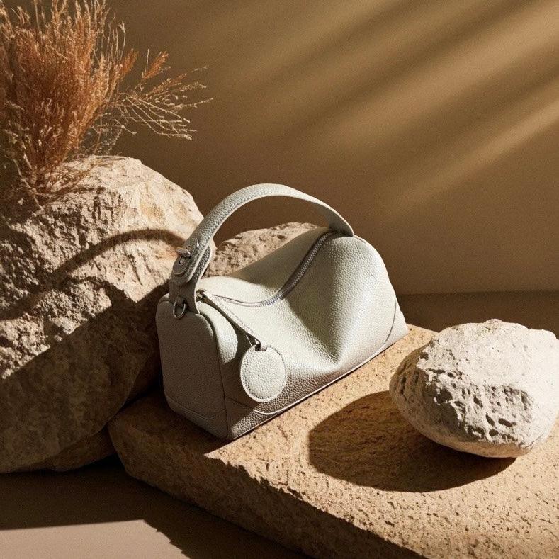 Beige leather handbag with top handle on stone slabs in warm sunlight