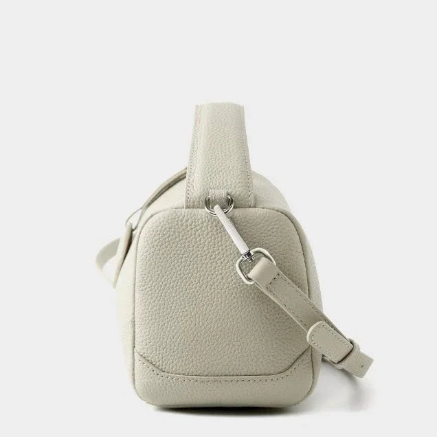 Side view of a light beige pebbled leather crossbody bag with adjustable strap