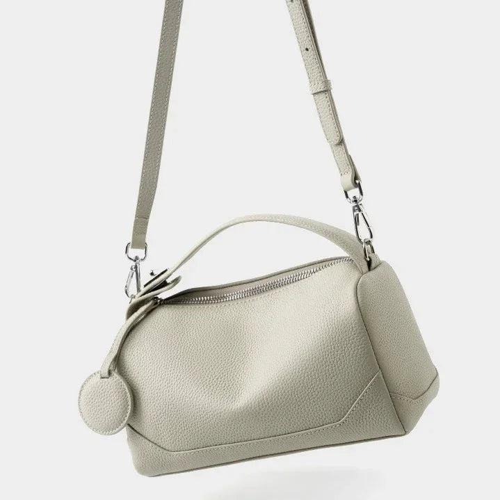 Beige leather crossbody bag with textured finish and adjustable strap on white background