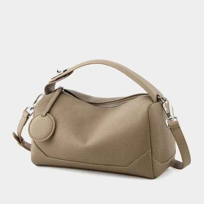 Taupe leather handbag with top handle, detachable strap, and zipper closure on white background